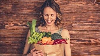 Eine Frau hält eine Papiertüte mit Gemüse in der Hand und lacht. 